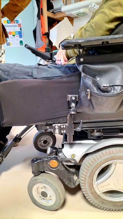Vue du profil gauche du fauteuil où se trouve la fixation (glissière dans laquelle se glisse le méplat auquel est soudé un tube carré)